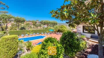 Außenterrasse der Villa Jaruco mit einem blauen Swimmingpool, gesäumt von gestreiften Sonnenliegen und umgeben von grünen Bäumen unter einem klaren blauen Himmel