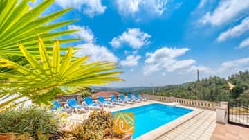 Privater Pool mit blauen Liegen und einem Palmwedel im Vordergrund an der Villa Santa Maria unter einem blauen Himmel mit vereinzelten Wolken.