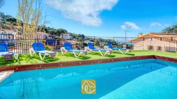 Außenpool mit strahlend blauem Wasser in der Villa Donna, ausgestattet mit vier weiß-blauen Sonnenliegen auf Kunstrasen unter einem klaren Himmel.