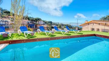 Außenpool mit strahlend blauem Wasser in der Villa Donna, ausgestattet mit vier weiß-blauen Sonnenliegen auf Kunstrasen unter einem klaren Himmel.