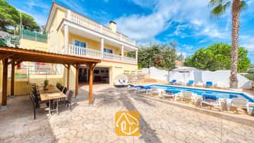 Privater Pool der Villa Ashley mit azurblauem Wasser und weißen Sonnenliegen. Die gelbe Villa besticht durch ihre Balkone mit weißer Balustrade sowie eine hölzerne Pergola, die zu Mahlzeiten im Freien auf dem Steinboden einlädt.