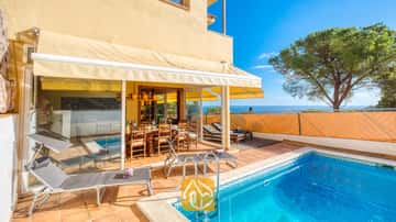 Der Swimmingpool und die Terrasse der Villa Santa Cristina bestechen durch Terrakotta-Fliesen, graue Sonnenliegen und einen schattigen Essbereich aus Holz unter einer gelben Markise – mit einem herrlichen Blick auf das Meer.