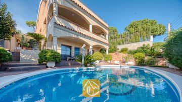 Ein geschwungener Swimmingpool mit Mosaikfliesenboden vor der mehrstöckigen Fassade der Villa Grace, die durch Steinbögen und Balkone unter einem klaren blauen Himmel besticht.