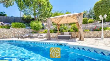Privater Pool der Villa Lorena mit blau gefliesten Rändern, einem beige Pavillon aus Stoff über den Sitzmöbeln im Freien, Natursteinmauern und umgebendem Grün.