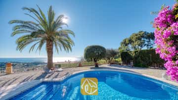 Der private Pool der Villa Gabriella besticht durch seine geschwungene Form, eine große Palme und graue Sonnenliegen auf einer Kiesterrasse, von der aus Sie unter strahlender Sonne einen herrlichen Blick auf das Meer genießen.