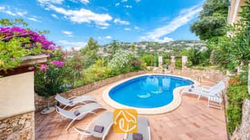 Privater Pool mit Sonnenliegen und gefliester Terrasse in der Villa Cleo in Spain, umgeben von Steinmauern und blühenden Büschen.