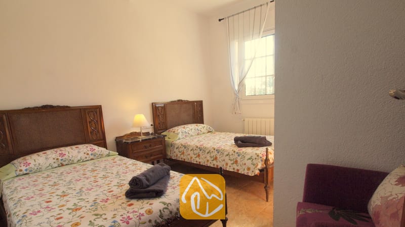 Schlafzimmer mit zwei Einzelbetten, dunklen Holzkopfteilen, mit Blumenmustern bedruckten Tagesdecken und gerollten grauen Handtüchern.
