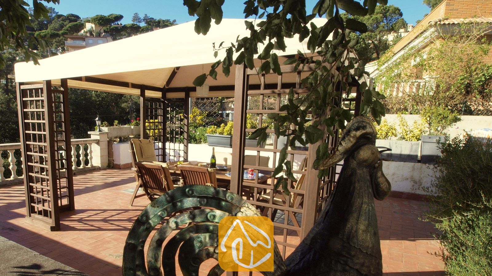 Holzpergola mit Stoffdach auf einer sonnigen Terrasse der Villa Noa, ausgestattet mit einem Esstisch im Freien und Stühlen im Schatten.