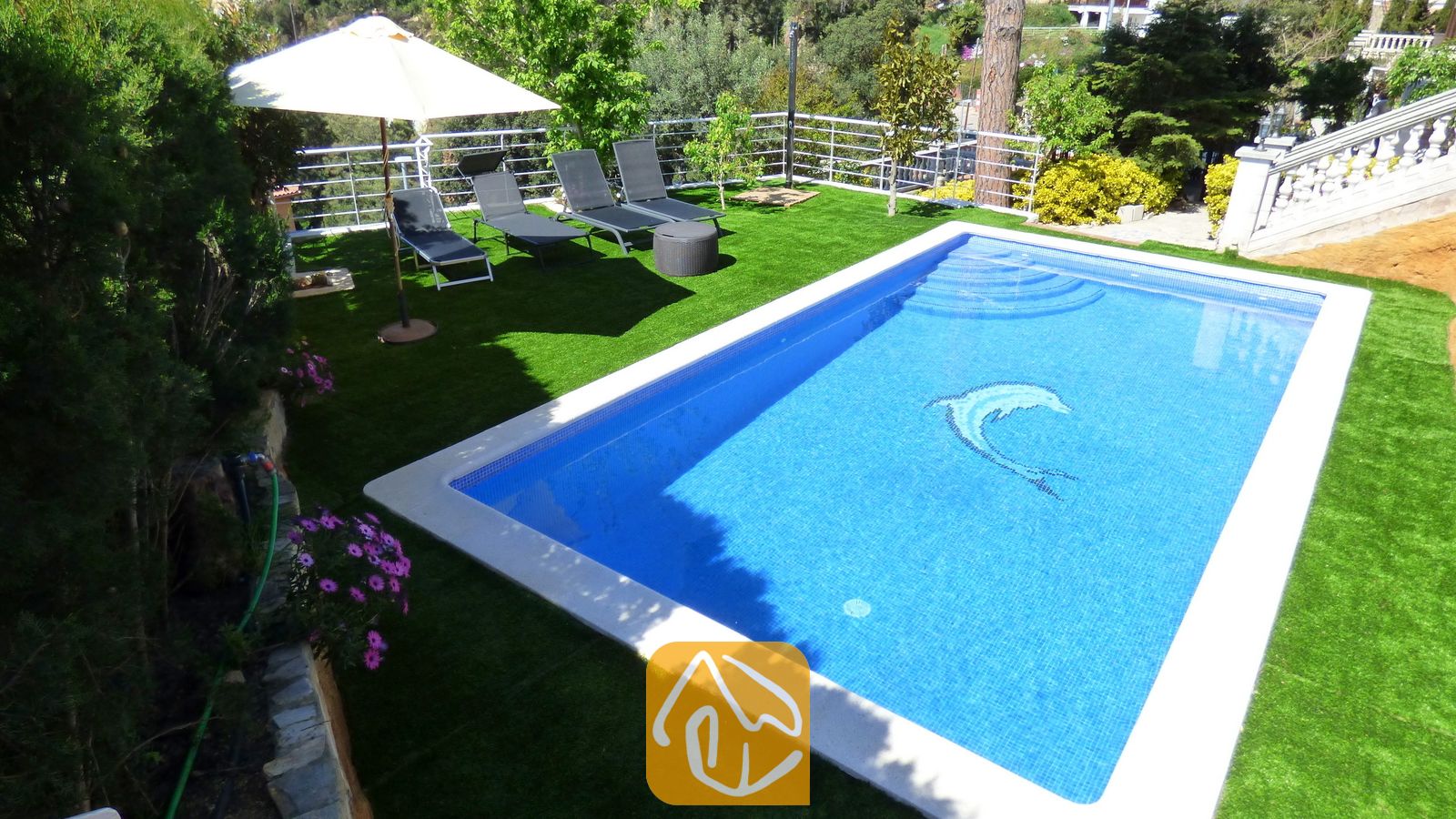Privater Pool mit Delfinmosaik in der Villa Noa, umgeben von Kunstrasen, Sonnenliegen und einem Sonnenschirm.