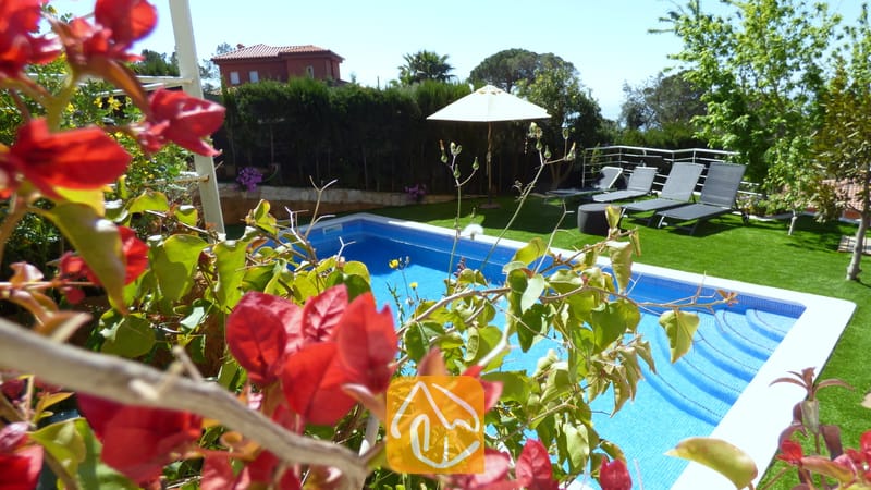 Der private Pool der Villa Noa, eingerahmt von roten Bougainvillea-Blüten, mit Sonnenliegen und einem weißen Sonnenschirm auf dem Rasen im Hintergrund.