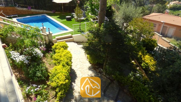 Ansicht von Villa Noa aus der Vogelperspektive mit einem steinernen Gartenweg, üppig grünen Büschen, blühenden Pflanzen und einem rechteckigen Swimmingpool, der von Kunstrasen umgeben ist.