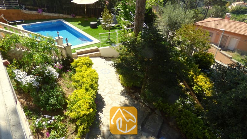 Ansicht von Villa Noa aus der Vogelperspektive mit einem steinernen Gartenweg, üppig grünen Büschen, blühenden Pflanzen und einem rechteckigen Swimmingpool, der von Kunstrasen umgeben ist.
