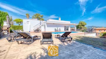 Privater Außenpool der Villa Yara, umgeben von dunklen Sonnenliegen auf einer gefliesten Terrasse unter einem strahlend blauen Himmel.