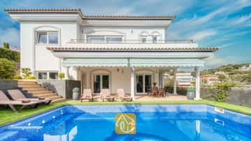 Außenansicht der Villa Madison mit einem blau gefliesten Swimmingpool, Sonnenliegen und einer überdachten Terrasse mit weißen Säulen vor einem klaren blauen Himmel