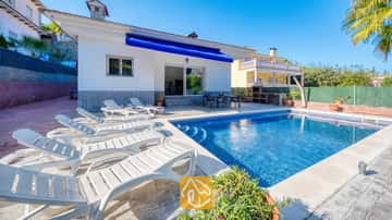 Ein privater Pool mit weißen Sonnenliegen entlang der gepflasterten Terrasse der Villa Zarita unter strahlend blauem Himmel.