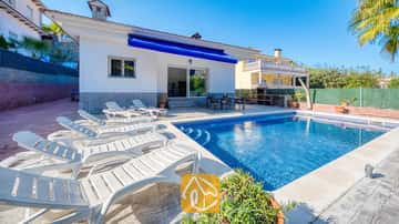 Ein privater Pool mit weißen Sonnenliegen entlang der gepflasterten Terrasse der Villa Zarita unter strahlend blauem Himmel.