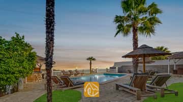 Der private Außenpool der Villa Tropicana, umgeben von Holzliegen, Palmen und Strohschirmen unter einem abendlichen Himmel.