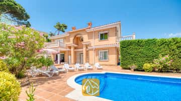 Privater Swimmingpool und Terrasse der Villa Primavera mit weißen Sonnenliegen, Terrakottafliesen und einer zweistöckigen, pfirsichfarbenen Fassade unter einem blauen Himmel.