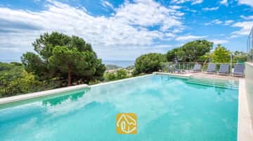 Privater Pool der Villa BellaVista mit türkisfarbenen Fliesen, einer durch Glas geschützten Sonnenterrasse mit grauen Liegen sowie einem herrlichen Blick auf das Meer und die Pinienwälder.