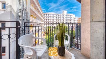 Balkon des Apartment Gaudi mit zwei weißen Plastikstühlen, einem kleinen Tisch mit einer Topfpflanze und einem Metallgeländer mit Blick auf die benachbarten weißen Gebäude.