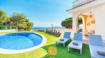 Privater Pool und blaue Holzsonnenliegen auf Kunstrasen an der Villa Ibiza mit Blick auf das weite Meer und die Bäume.