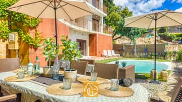 Esstisch im Freien, gedeckt mit gewebten Platzdeckchen, Glasbechern und Zitronenbäumchen im Topf, in der Villa Sunny Beach mit Blick auf einen Swimmingpool und eine Terrasse.