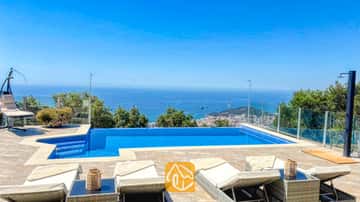 Privater Swimmingpool und geflieste Terrasse der Villa VistaMar mit weißen Sonnenliegen, Glasgeländern und einem weiten Blick auf die Küste unter einem blauen, wolkenlosen Himmel.